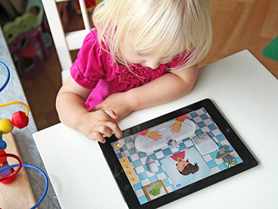 Little girl playing Ella&rsquo;s handwashing adventure app on a tablet (photo)