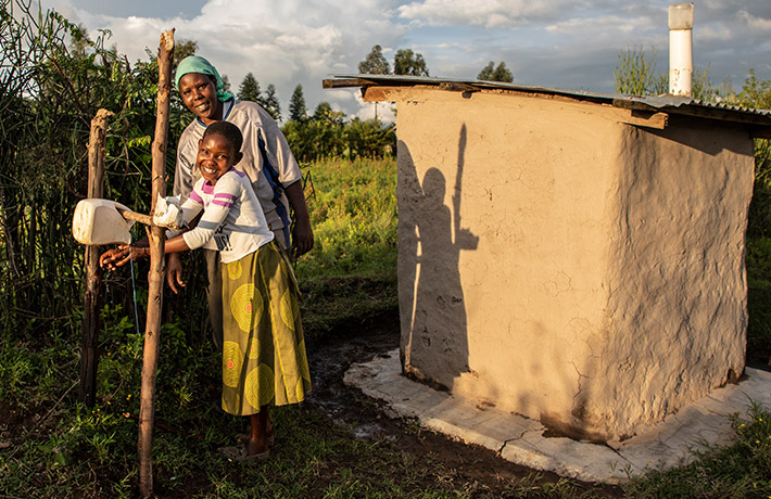 Kid using a tippy tap handwashing station next to her mother (photo)